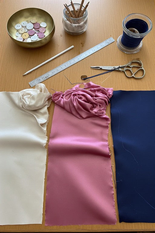 Vivere fabric swatches in ivory, rose, and navy with tailoring tools — our craft
